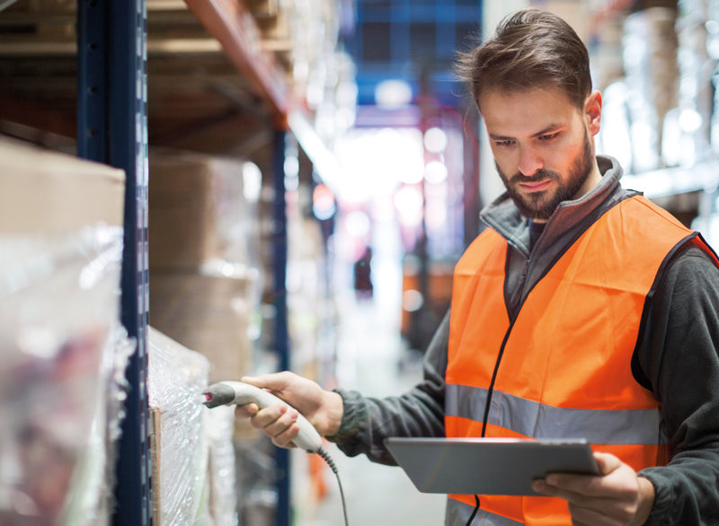 Man with barcode scanner and a tablet scanning stock in a warehouse. Image for SafeContractor Website